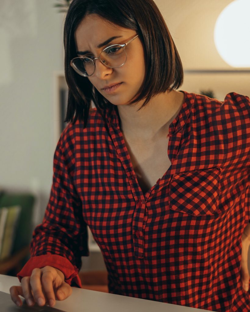 Beautiful woman having back and neck pain while using laptop at home